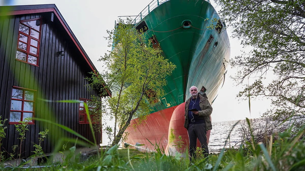 homem acorda e pela janela vê no seu jardim um enorme navio cargueiro